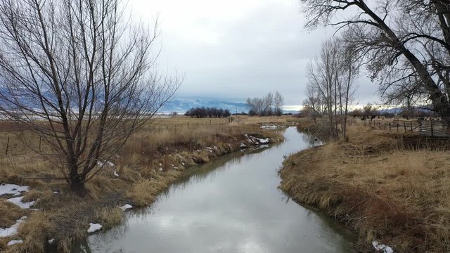 Aerial-Flying low and slow along slow moving winter stream on an overcast winter day through rural countryside