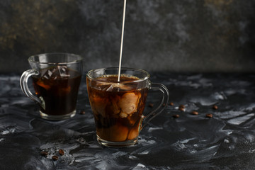  Two transparent cups of cold coffee with milk. Iced coffee.Stream of milk. Copy space. Close up. Milk explosion in iced coffee.