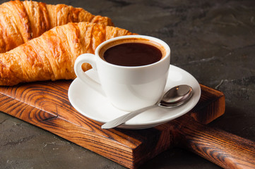 Espresso in a white cup and two croissants on dark background, on a wooden board