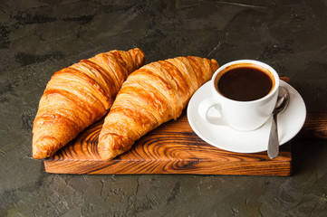 Espresso in a white cup and two croissants on a dark background, on wooden board, place for text, view from the top