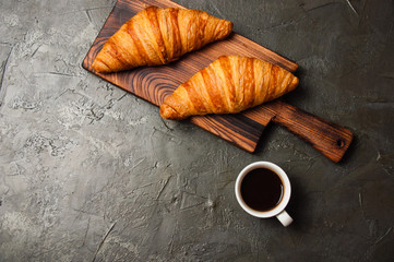 Fototapeta na wymiar Strong espresso or ristretto coffee in white cup and two tasty croissants on a dark concrete background, on a wooden board, flat lay. Concept for breakfast, coffee break or business lunch.