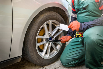 Mechanic in robe fixing car wheel. Car service concept with mechanic repairing car