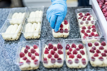 Confectioner decorating delicious desserts with raspberry on factory. Amazing delicious food