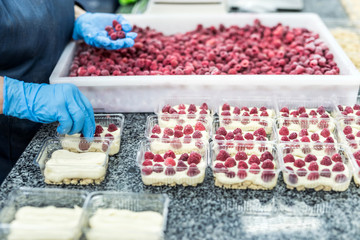 Confectioner decorating delicious desserts with raspberry on factory. Amazing delicious food