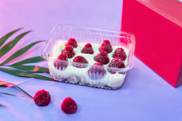 Delicious dessert in plastic package with raspberry on table and pink wrapping close up. Food concept