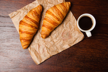 Delicious croissants and ristretto coffee in a white cup on vintage crumpled craft paper, on dark wooden tabletop