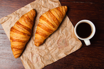Delicious croissants and ristretto coffee in a white cup on vintage crumpled craft paper, on dark wooden tabletop