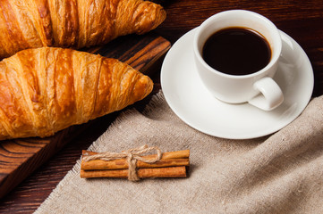 Concept delicious breakfast. Cinnamon croissants, cup of coffee and a linen napkin on a wooden table, top view, flat lay, rustic style