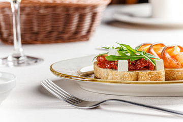 Italian cuisine. Three bruschettas on a white plate with cheese, cherry tomatoes, basil, loss, sun-dried tomatoes, feta. Female hand holds tapas. background image, copy space text