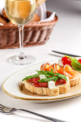Italian cuisine. Three bruschettas on a white plate with cheese, cherry tomatoes, basil, loss, sun-dried tomatoes, feta. Female hand holds tapas. background image, copy space text