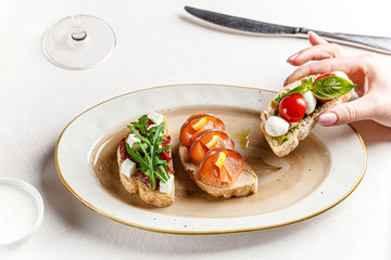 Italian cuisine. Three bruschettas on a white plate with cheese, cherry tomatoes, basil, loss,...