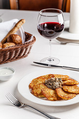 Ukrainian cuisine. A grated potato dish of deruny, draniki grated on a white plate with red wine. Serving dishes in a restaurant in a white plate. background image, copy space text