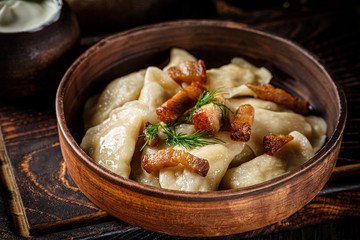 Ukrainian cuisine. vareniki with potatoes and fried pork fat - cracklings. Serving dishes in a Ukrainian style restaurant with sour cream on a wooden background. background image, copy space text