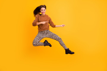 Fototapeta na wymiar Full length photo of pretty funny lady jump high indicating fingers empty space advising final season sales wear fluffy pullover leopard pants footwear isolated yellow color background