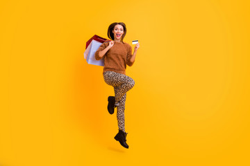 Fototapeta na wymiar Full length profile photo of funny lady jump high carry packs shopaholic hold plastic credit card wear casual fluffy pullover leopard trousers boots isolated yellow color background