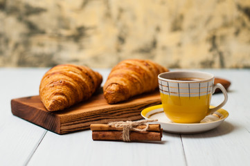 Tasty croissants and coffee in yellow cup with cinnamon on a light background