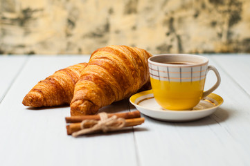 Espresso coffee in vintage yellow cup, croissants and cinnamon on a light background, breakfast concept