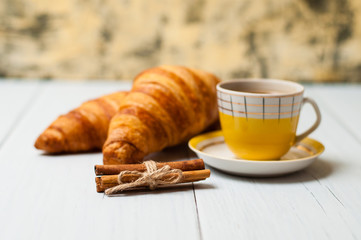 Espresso coffee in vintage yellow cup, croissants and cinnamon on a light background, breakfast concept