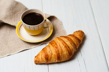 Espresso in vintage yellow cup with saucer and spoon, on linen napkin croissant on light background, concept of lunch