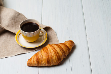 Espresso in vintage yellow cup with saucer and spoon, on linen napkin croissant on light background, concept of lunch