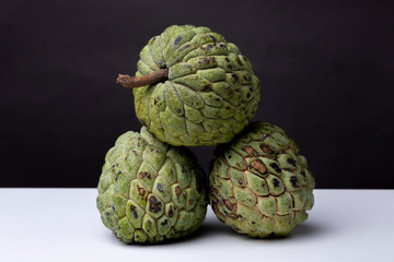 Three Sugar-apple fruits or 'Fruta de Conde' [Earl Fruit] as it is known in Brazil as a lot together on a white studio surface against a dark background