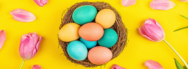 Stylish background with colorful easter eggs isolated on yellow background with pink tulip flowers. Flat lay, top view, mockup, overhead, template
