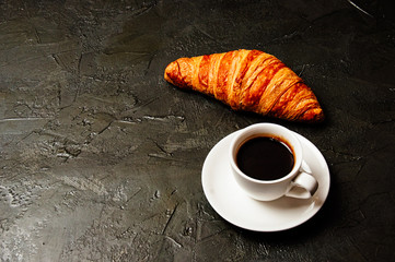 Croissant and espresso on dark gray concrete background with a place to insert text from the left. The concept of a delicious breakfast, business lunch or coffee break.