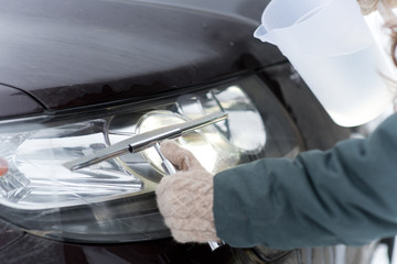 Girl cleans the headlights of a car before the road trip with the help of warm water