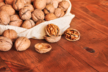 Walnut kernels and whole walnuts on rustic old wooden table, walnuts in a reusable cloth bag