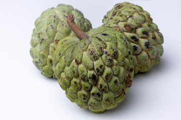 Close up of three Sugar-apples or 'Fruta de Conde' [Earl Fruit] as it is known in Brazil forming a heart shape on a white background surface