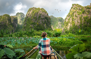 Woman traveling by boat on river amidst the scenic green karst mountains in Ninh Binh province,...