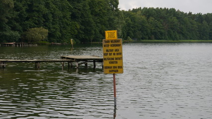 Widok na jezioro z pomostem, na tabliczce napis 
