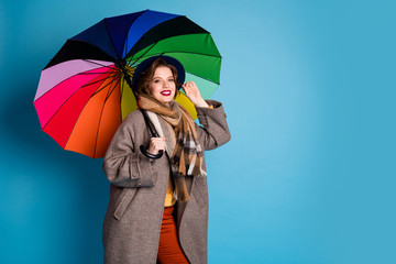 Photo of pretty traveler lady hold colorful parasol walking down street wear stylish casual long grey coat jumper orange pants hat plaid scarf isolated blue color background