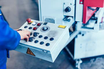 Worker operating saw machine for cutting steel profiles in a factory