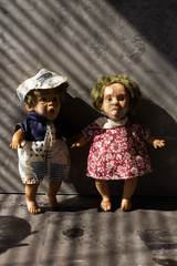 Old, scary, ugly dolls in front of concrete wall.