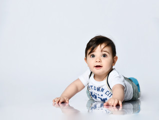 Little toddler in t-shirt with inscriptions, jeans with suspenders. He is laying on floor isolated on white background. Close up