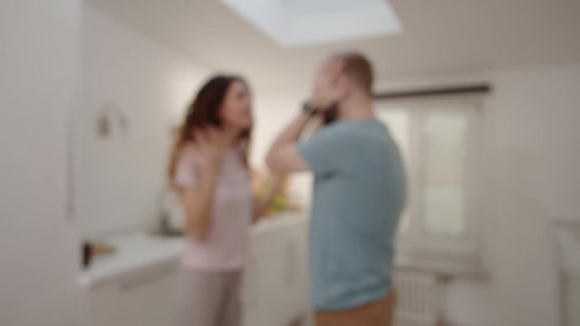 Thigh-up arc shot with blurred effect of husband and wife standing face to face and quarreling at home, nagging woman shouting, reproaching and gesticulating while man is listening and grabbing head