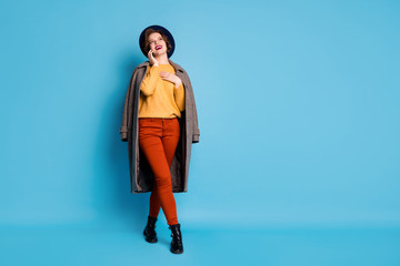 Full length photo of funny lady traveler speaking telephone friends tell address shopping center wear season long grey coat sweater pants hat boots isolated blue color background