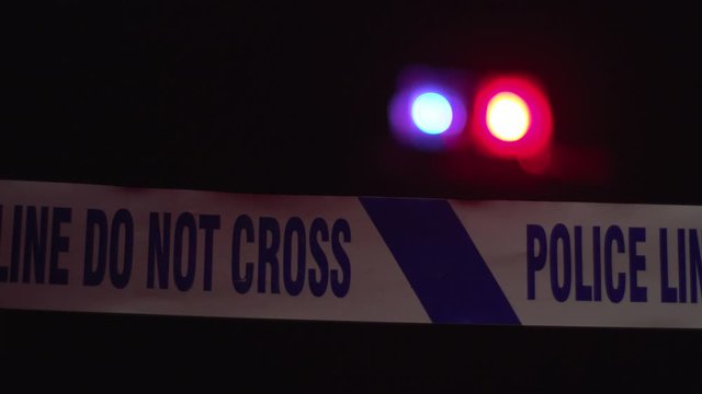 Police tape - crime scene cordon saying Do not Cross. Night time. Red & Blue sirens in the background. Tracking Shot