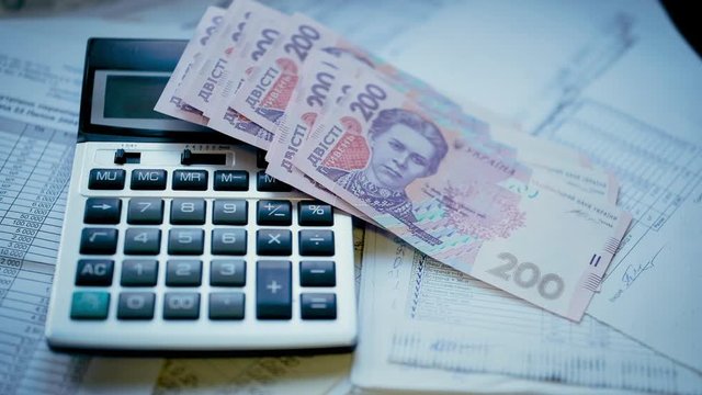 200 Ukrainian hryvnias fall next to the calculator on accounting documents and reports.