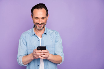 Portrait of positive cheerful man use smart phone chatting blog post follow bloggers share social media information wear good looking clothing isolated over violet color background