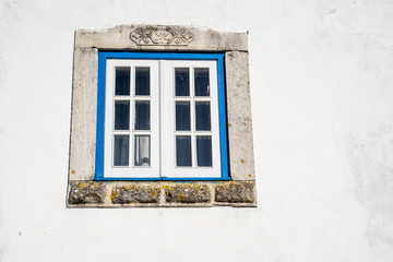 Old, ornate window with a painted blue frame and white wall. Traditional in Obidos, Portugal