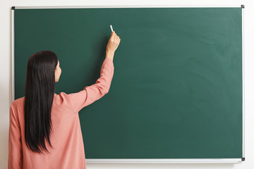 Female teacher writing on blackboard in classroom
