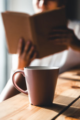Woman in the morning drinks coffee and reads old book in a white shirt. Education, drink. manicure