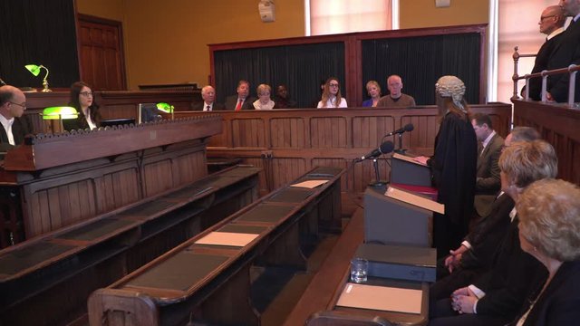Female Barrister / Lawyer addressing the Jury in Court. She is wearing a wig & gown in the Courtroom. Wide Shot
