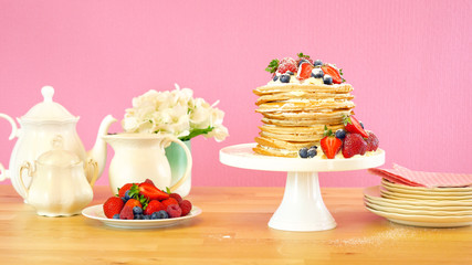 Shrove Pancake Tuesday, last day before Lent, stack of pancakes cake prepared with layers of whipped cream and fresh berries against modern pink background.