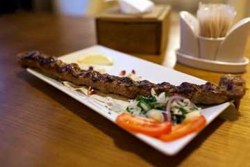 Lula kebab meat dish with vegetables served in restaurant on wooden table. Barbecue