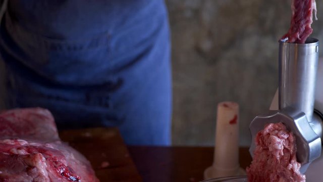 beautiful mature woman in pink sweater and gray economic apron cuts large piece of pork into pieces with knife and ax. girl puts small pieces in meat grinder and grinds them into minced meat