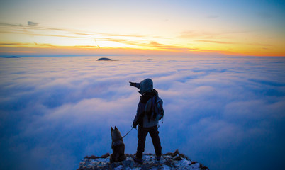 A shot of a landscape with inverse weather. Silhouette of hiker with dog looking into the landscape. The tourist cannot see his face.