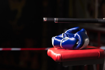 Pair of blue Boxing gloves lies on a red chair outside the ring on a dark background. Selective...